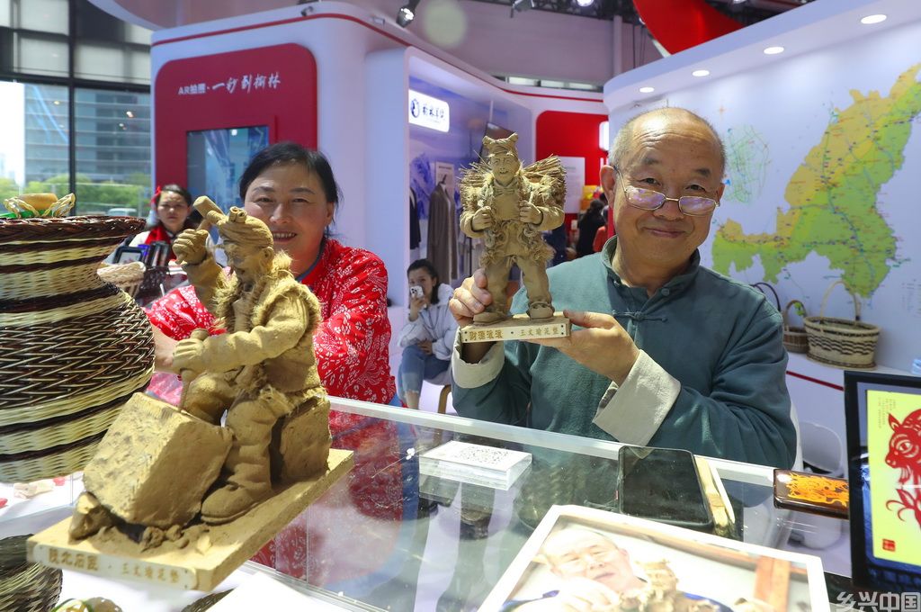 5月12日，来自陕西榆林的农民艺术家王文瑜（右）展示他的泥塑艺术作品《财源滚滚》。