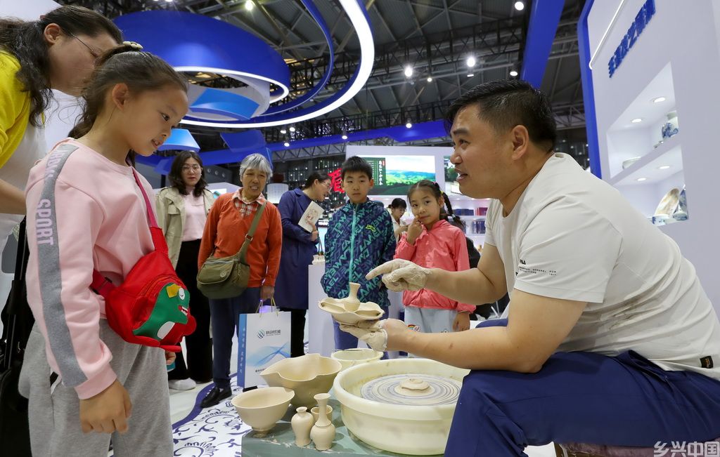 5月12日，江西景德镇展台的工作人员（右）向参观者介绍瓷器制作的步骤。